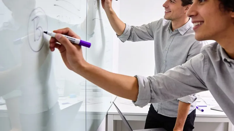 Founders sketching an idea on a glass wall in a small workspace.